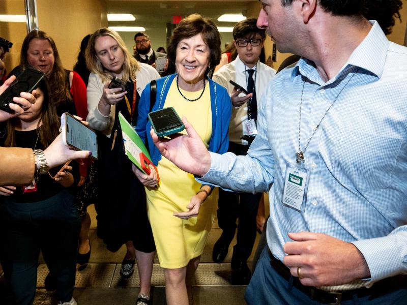 Sen. Susan Collins walks in a hallway surrounded by reporters